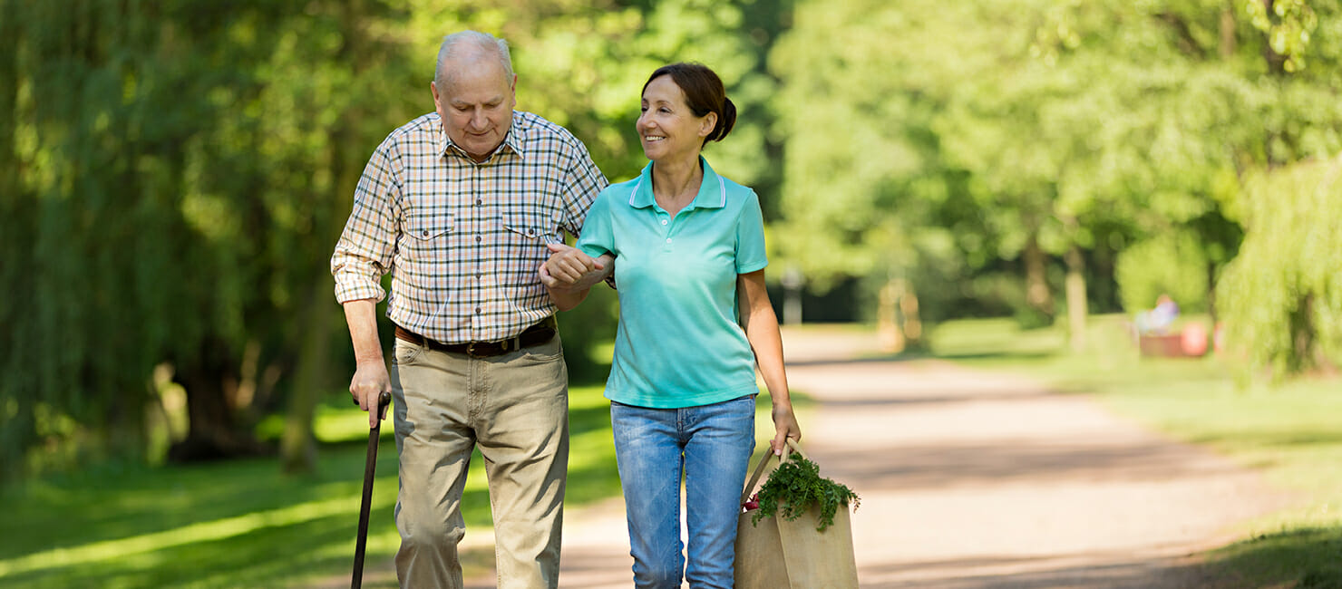 Elderly man walking wiht care aid bringing home groceries